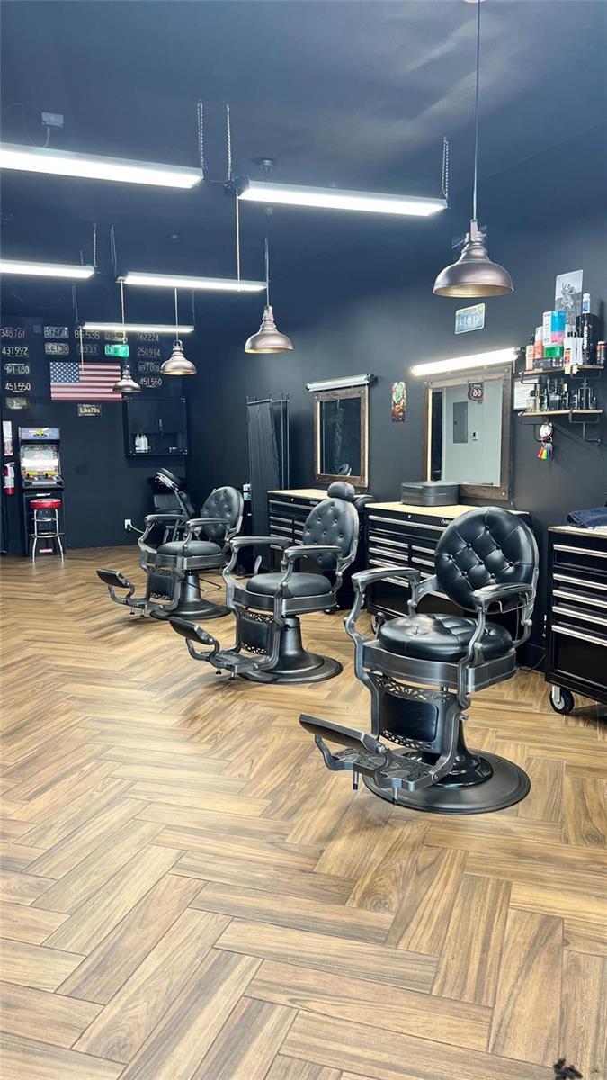 A barbershop interior features three black leather chairs, dark walls, and wood-patterned flooring — 20th Street, Boca Raton FL 33431, BOCA RATON, FL
