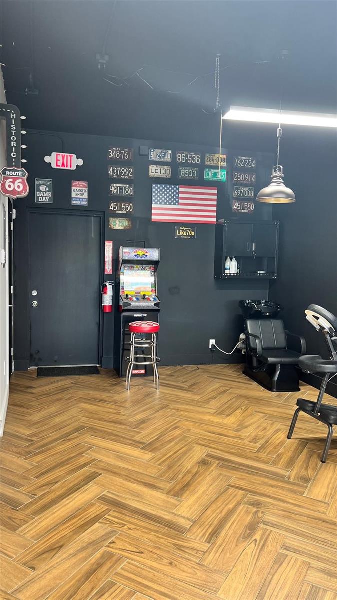 A barbershop interior features a black wall with license plates, an arcade machine, and flooring — 20th Street, Boca Raton FL 33431, BOCA RATON, FL