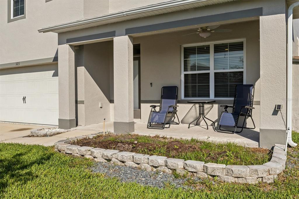 A covered concrete porch features two lounge chairs, a small table, and a stone planter — 323 HARBOUR WAY, MULBERRY, FL