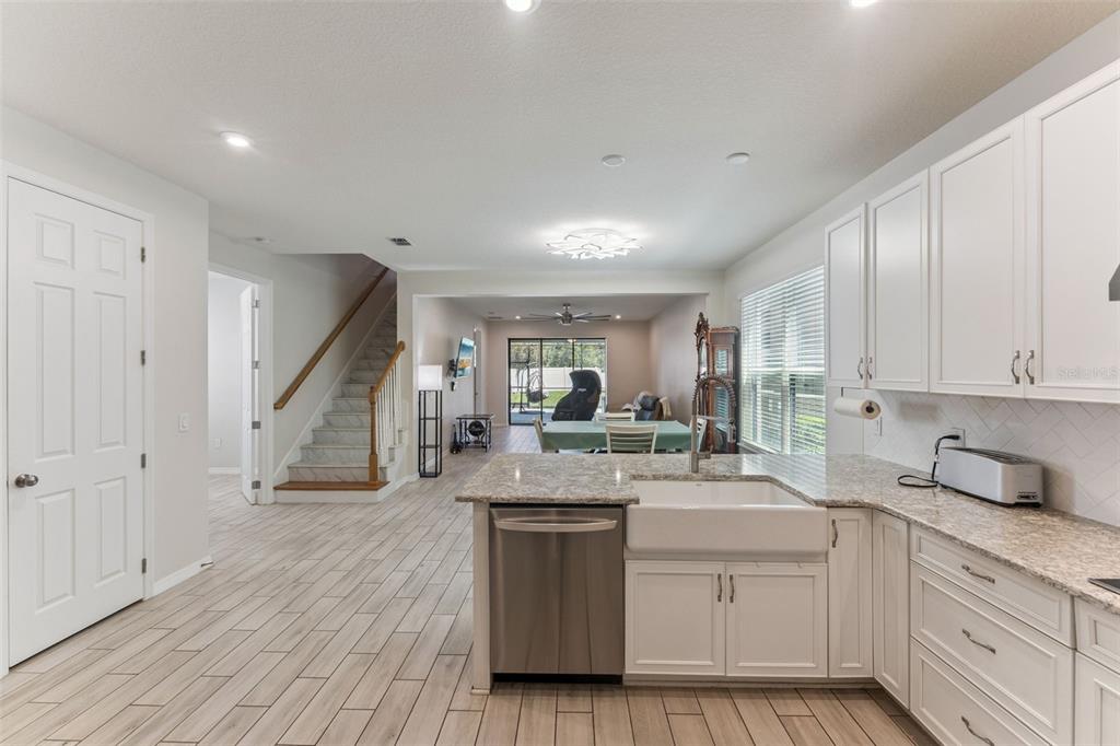 A kitchen with white cabinets and a farmhouse sink overlooks a living area and stairs — 1287 VERDANT GLADE PLACE, WINTER PARK, FL