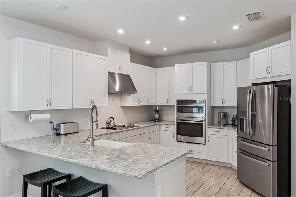 A kitchen features white cabinets, granite countertops, stainless steel appliances, and a breakfast bar — 1287 VERDANT GLADE PLACE, WINTER PARK, FL