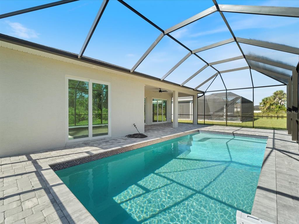 A swimming pool with a paved deck is enclosed by a screened lanai behind a house — 13356 RAYBURN LANE, PORT CHARLOTTE, FL