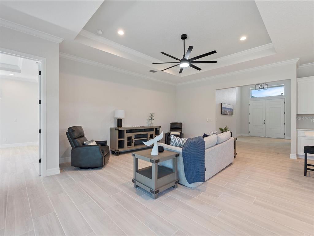 A living room features light wood-look tile flooring, a tray ceiling, and a modern ceiling fan — 13356 RAYBURN LANE, PORT CHARLOTTE, FL