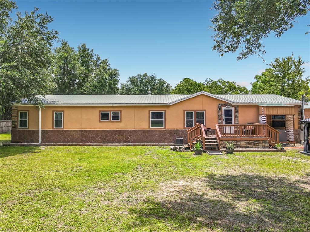 A single-story house with tan stucco, stone skirting, a metal roof, and a wooden deck — 5118 PECAN AVENUE, BUNNELL, FL
