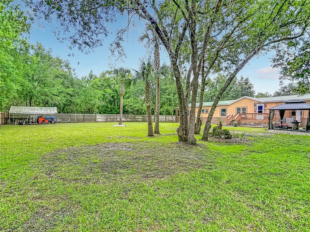 A large grassy backyard features mature trees, a wooden deck, and a metal carport — 5118 PECAN AVENUE, BUNNELL, FL