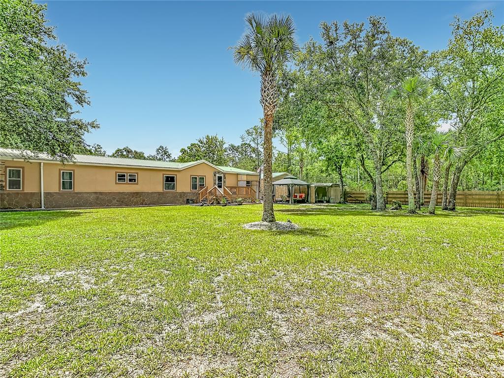 A tan house with a metal roof sits behind a large lawn with palm trees — 5118 PECAN AVENUE, BUNNELL, FL