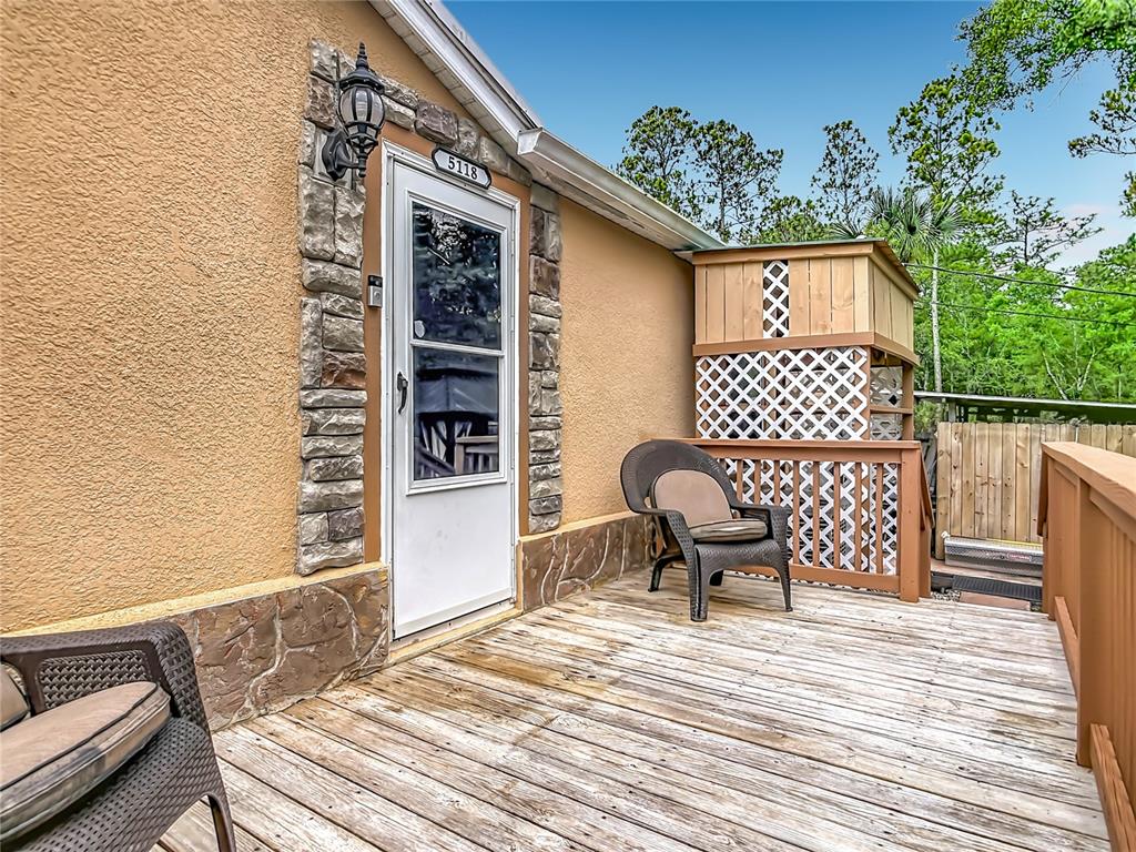 A wooden deck features a stone-trimmed doorway, a wicker chair, and a lattice privacy screen — 5118 PECAN AVENUE, BUNNELL, FL