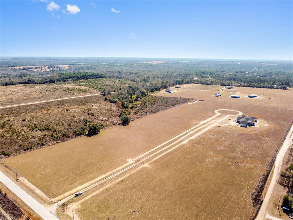 An aerial view shows a large, open field with a single house and a dirt driveway — 4237 ROYAL SKY (LOT 5) COURT, BROOKSVILLE, FL