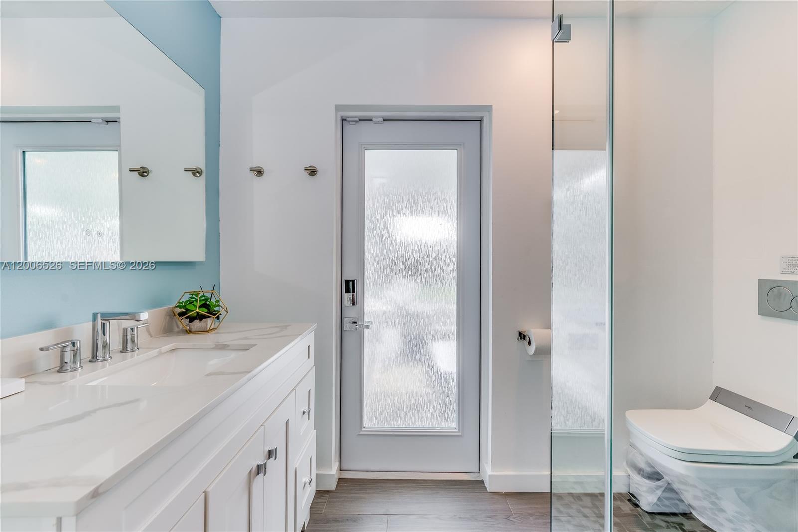 A modern bathroom features a white vanity, a frosted glass door, and a wall-mounted toilet — 4212 Van Buren St # 0, Hollywood FL 33021, HOLLYWOOD, FL