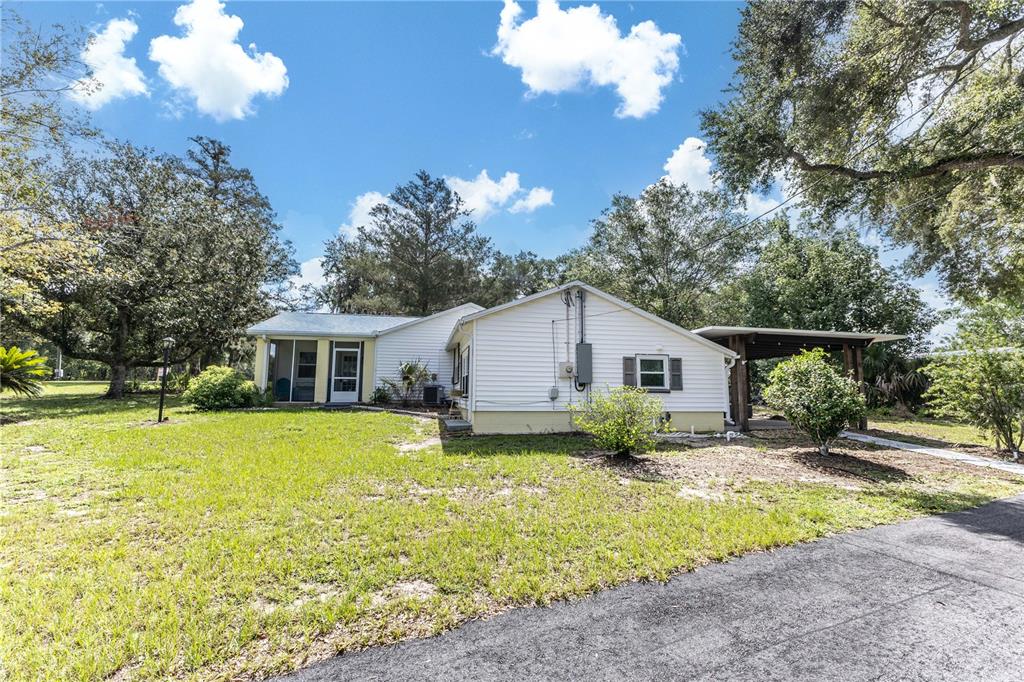 A single-story house with white siding, a screened porch, and a carport on a lawn — 11302 SE HIGHWAY 42 HIGHWAY, SUMMERFIELD, FL