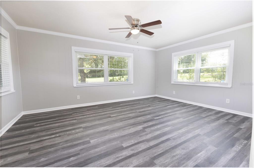 A bright, empty room features gray wood-look flooring, light gray walls, and a ceiling fan — 11302 SE HIGHWAY 42 HIGHWAY, SUMMERFIELD, FL