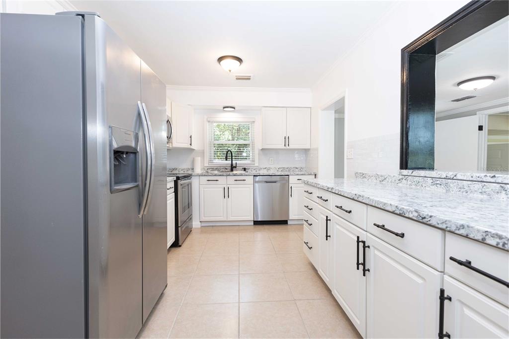 A kitchen features white cabinets, granite countertops, stainless steel appliances, and light tile flooring — 11302 SE HIGHWAY 42 HIGHWAY, SUMMERFIELD, FL