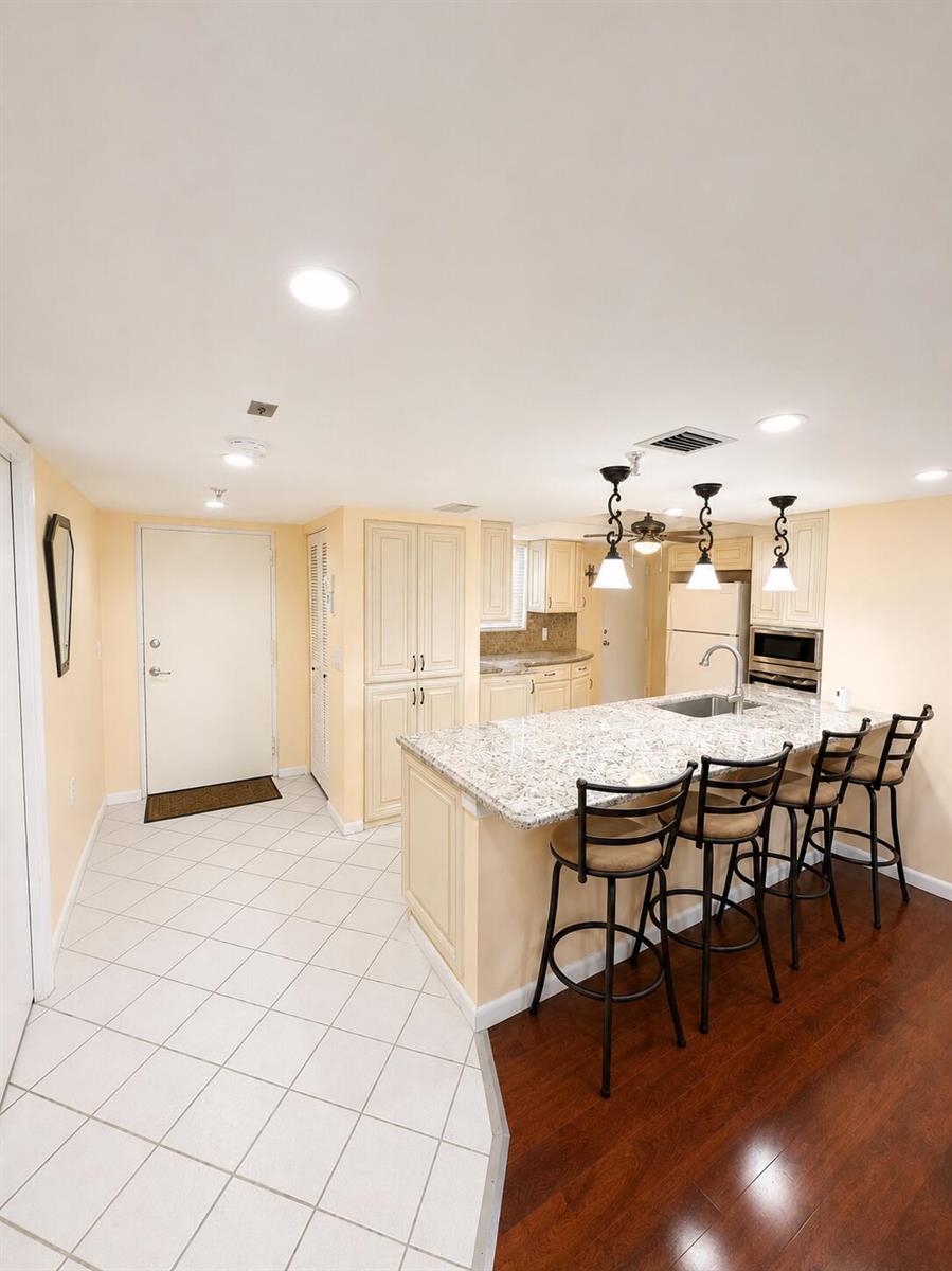 A kitchen with cream cabinets, granite countertops, a breakfast bar, and mixed flooring — 6500 NW 2nd Avenue # 512, Boca Raton FL 33487, BOCA RATON, FL
