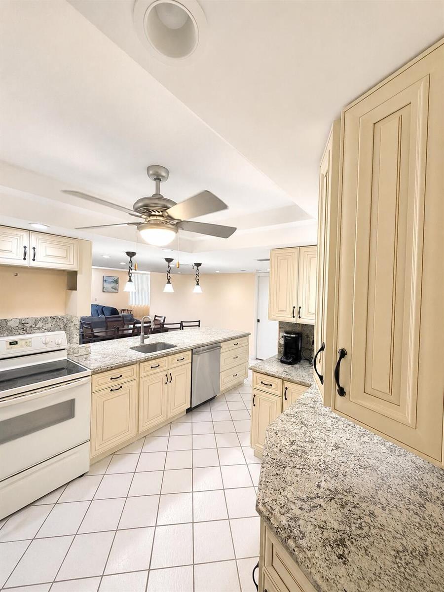 A kitchen with cream-colored cabinets, granite countertops, white appliances, and tiled flooring — 6500 NW 2nd Avenue # 512, Boca Raton FL 33487, BOCA RATON, FL