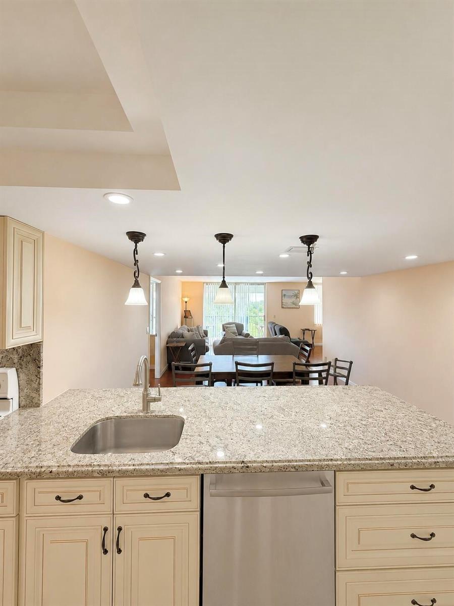 A kitchen island with a granite countertop and sink overlooks an open dining and living area — 6500 NW 2nd Avenue # 512, Boca Raton FL 33487, BOCA RATON, FL