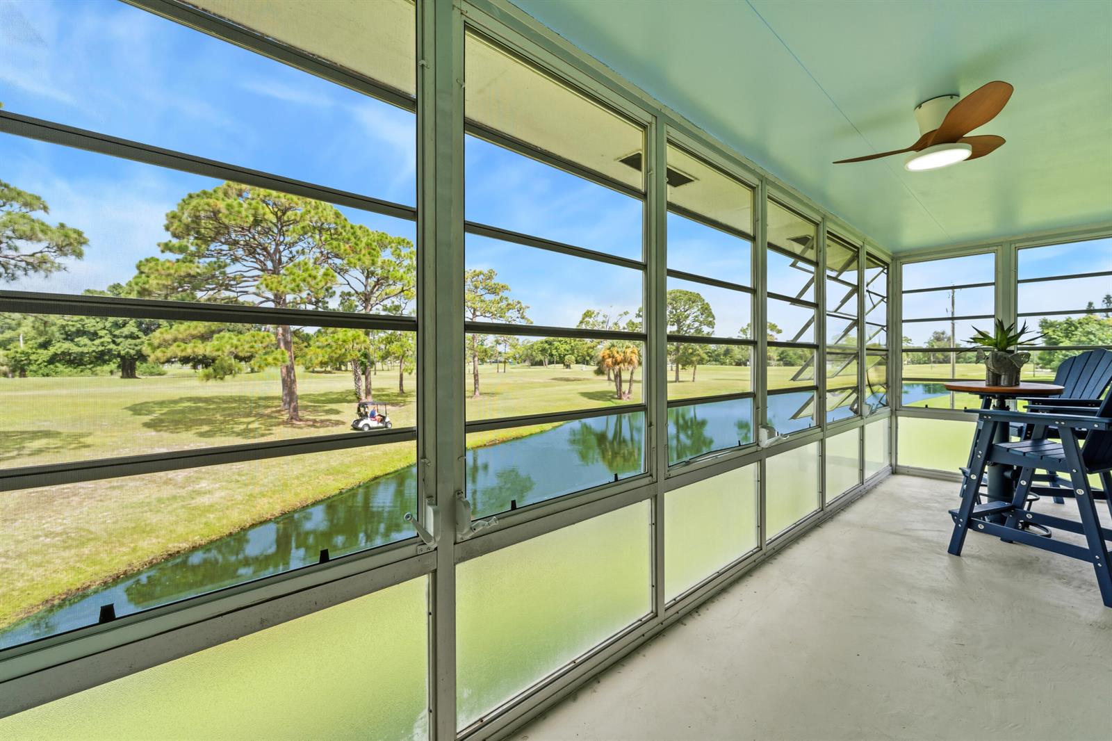 A screened-in porch overlooks a golf course pond with blue chairs and a ceiling fan — 1225 NW 21st Street # 1708, Stuart FL 34994, STUART, FL