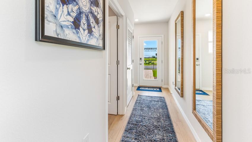 A hallway with light wood flooring, a blue runner rug, and two large wall mirrors — 18113 GANDER TERRACE, LAKEWOOD RANCH, FL