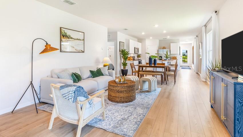 A bright open-concept living room features a light-colored sofa, a blue rug, and a kitchen — 18113 GANDER TERRACE, LAKEWOOD RANCH, FL