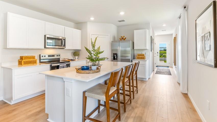 A modern kitchen features white cabinetry, a central island with bar stools, and stainless appliances — 18113 GANDER TERRACE, LAKEWOOD RANCH, FL