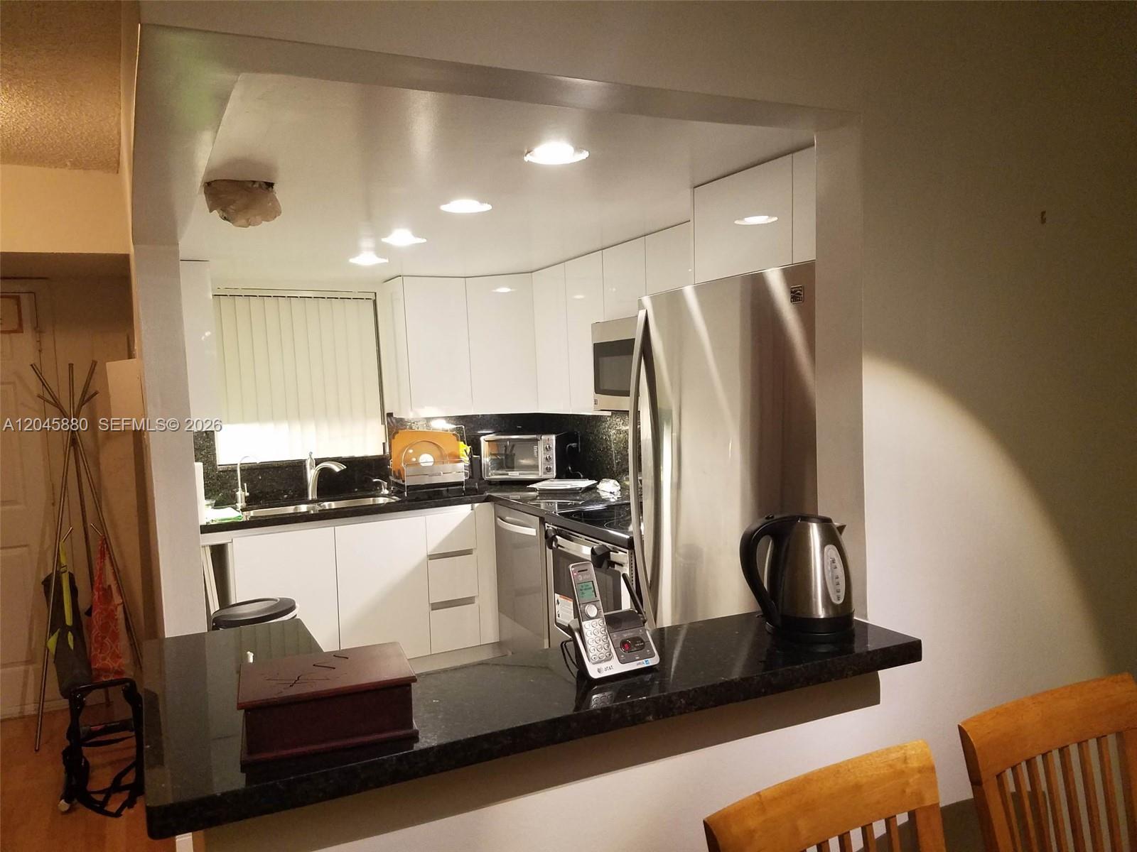 A kitchen features white cabinets, black countertops, stainless steel appliances, and a breakfast bar — 9371 Fontainebleau Blvd # I208, Miami FL 33172, MIAMI, FL