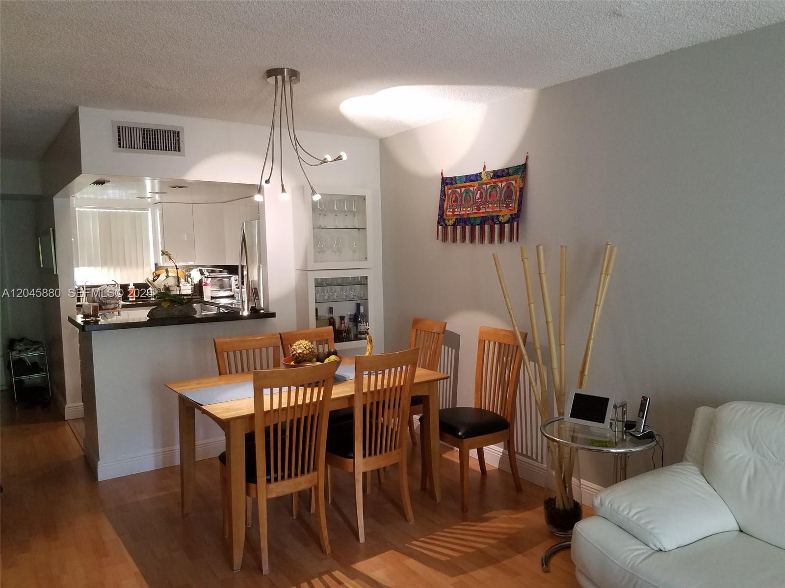 A dining area features a wooden table, chairs, a modern light fixture, and a wall tapestry — 9371 Fontainebleau Blvd # I208, Miami FL 33172, MIAMI, FL