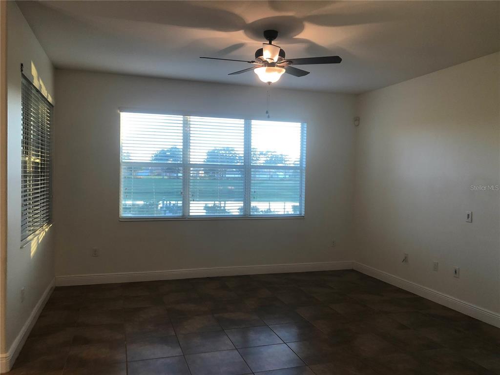 An empty room features tiled flooring, a ceiling fan, and large windows overlooking a lake — 2360 EAGLE TALON COURT, KISSIMMEE, FL