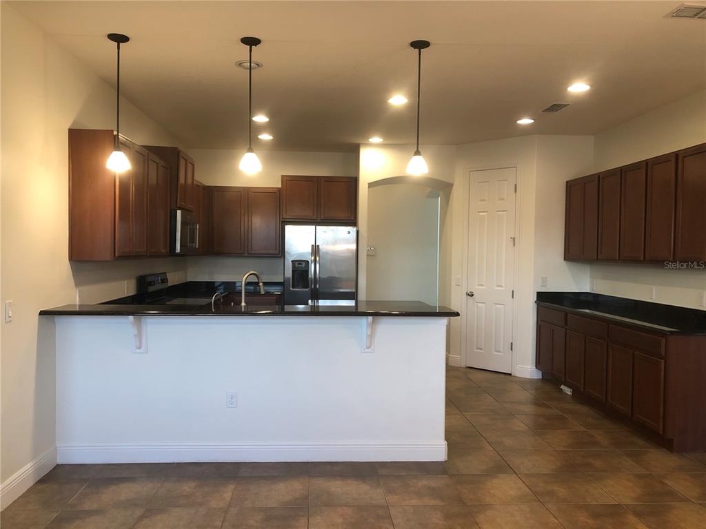 A kitchen features dark wood cabinets, black countertops, stainless steel appliances, and three pendant lights — 2360 EAGLE TALON COURT, KISSIMMEE, FL