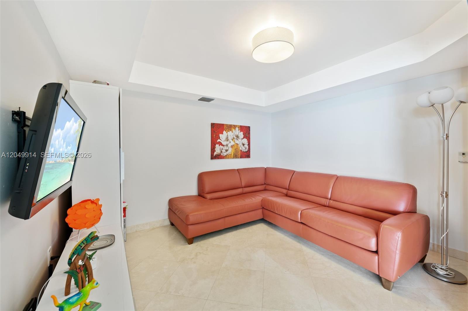 A living room features a coral-colored sectional sofa, a wall-mounted television, and tile flooring — 16400 Collins Ave # 1644, Sunny Isles Beach FL 33160, SUNNY ISLES BEACH, FL