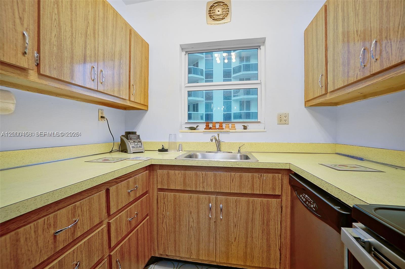 A kitchen features wood-grain cabinets, yellow countertops, a stainless steel sink, and a window — 4747 Collins Ave # 1108, Miami Beach FL 33140, MIAMI BEACH, FL