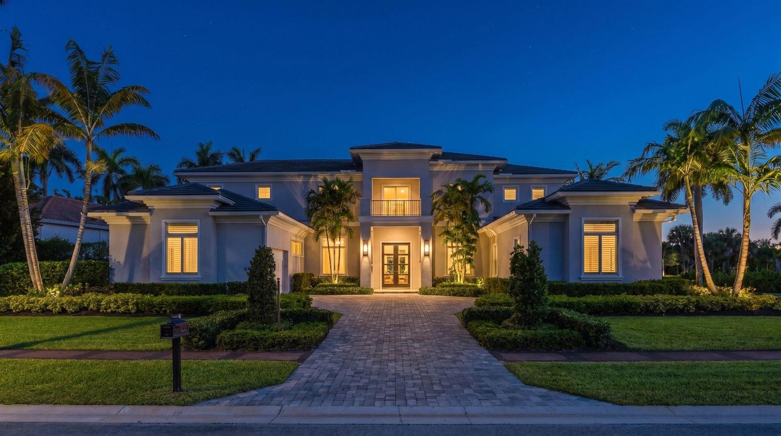A two-story luxury home with a paved driveway, palm trees, and illuminated exterior at dusk — 17661 Scarsdale Way, Boca Raton FL 33496, BOCA RATON, FL