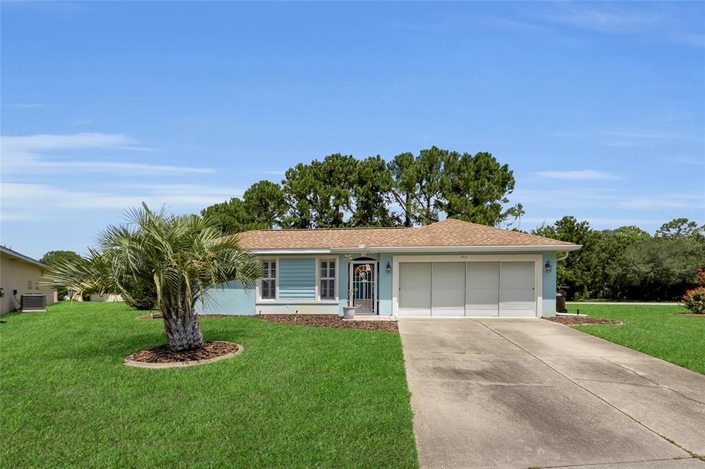 A light blue single-story house with a palm tree, concrete driveway, and attached garage — 7221 SW 115TH PLACE, OCALA, FL