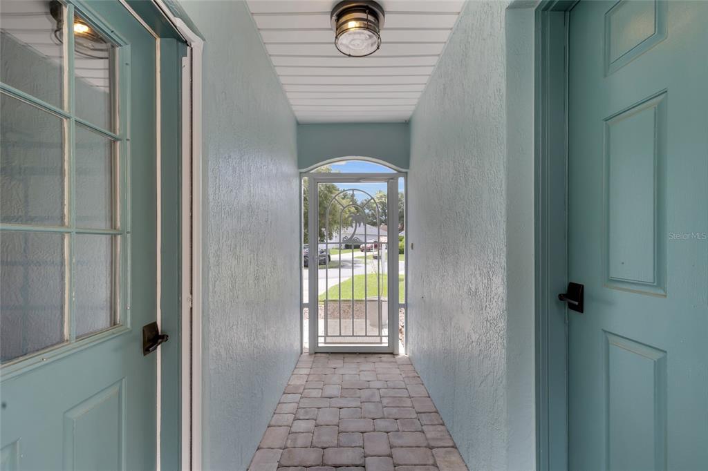 A covered entryway features light blue walls, a paver floor, and a decorative screen door — 7221 SW 115TH PLACE, OCALA, FL