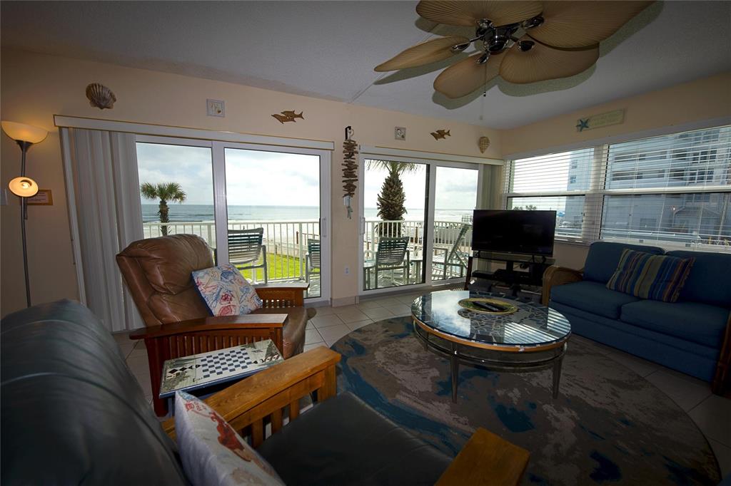 A living room with a ceiling fan, tiled floors, and sliding glass doors overlooking the ocean — 1571 S ATLANTIC AVENUE UNIT 208, NEW SMYRNA BEACH, FL