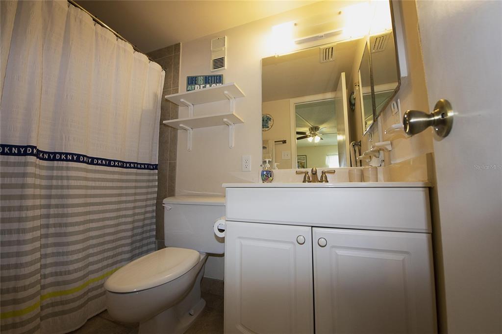 A bathroom features a white vanity, a toilet, and a shower with a striped curtain — 1571 S ATLANTIC AVENUE UNIT 208, NEW SMYRNA BEACH, FL