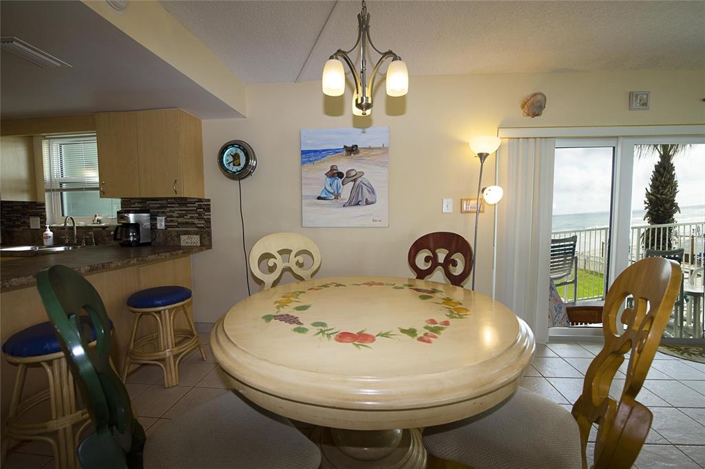 A dining area with a round painted table, wooden chairs, and a view of the ocean — 1571 S ATLANTIC AVENUE UNIT 208, NEW SMYRNA BEACH, FL