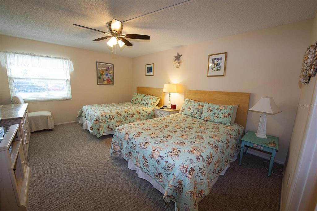 A bedroom features two beds with seashell-patterned quilts, a ceiling fan, and a window — 1571 S ATLANTIC AVENUE UNIT 208, NEW SMYRNA BEACH, FL
