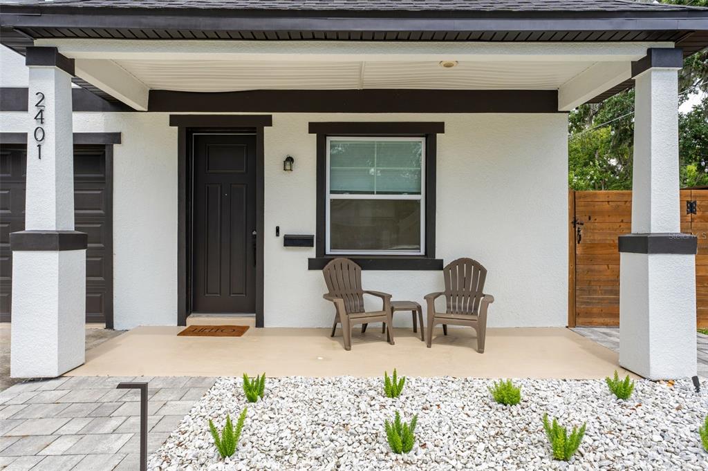 A covered front porch features a dark door, a window, and two chairs on a concrete floor — 2401 AMHERST AVENUE, ORLANDO, FL