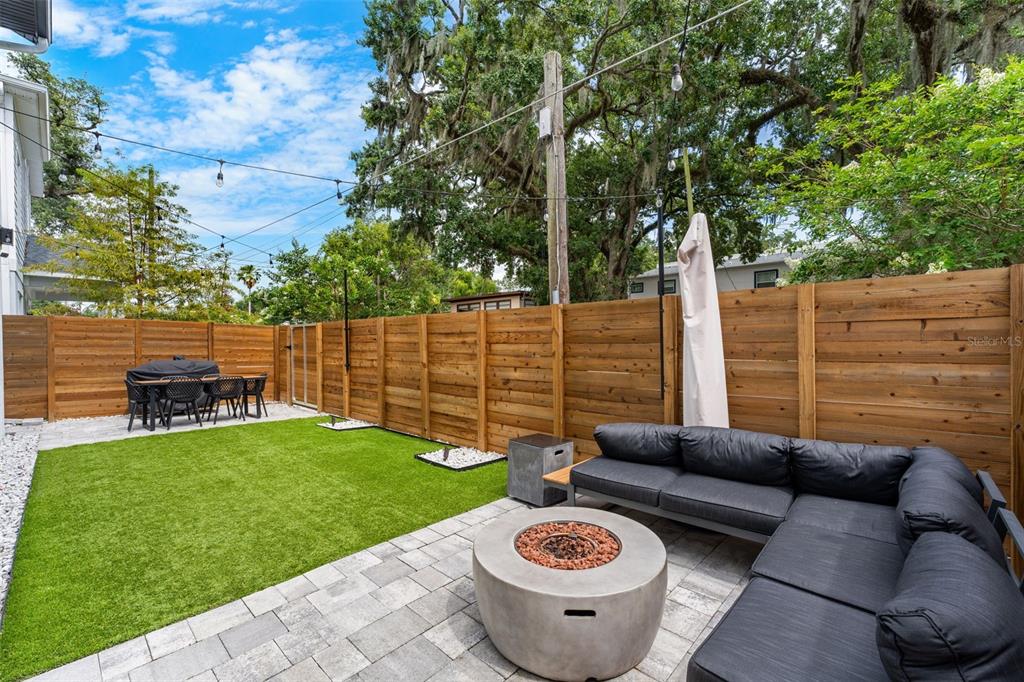A backyard features a paver patio with a fire pit, sectional sofa, and artificial turf — 2401 AMHERST AVENUE, ORLANDO, FL