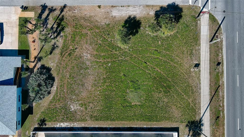 An aerial view shows a vacant, rectangular grassy lot situated between a road and buildings — 0 S ATLANTIC AVENUE, NEW SMYRNA BEACH, FL