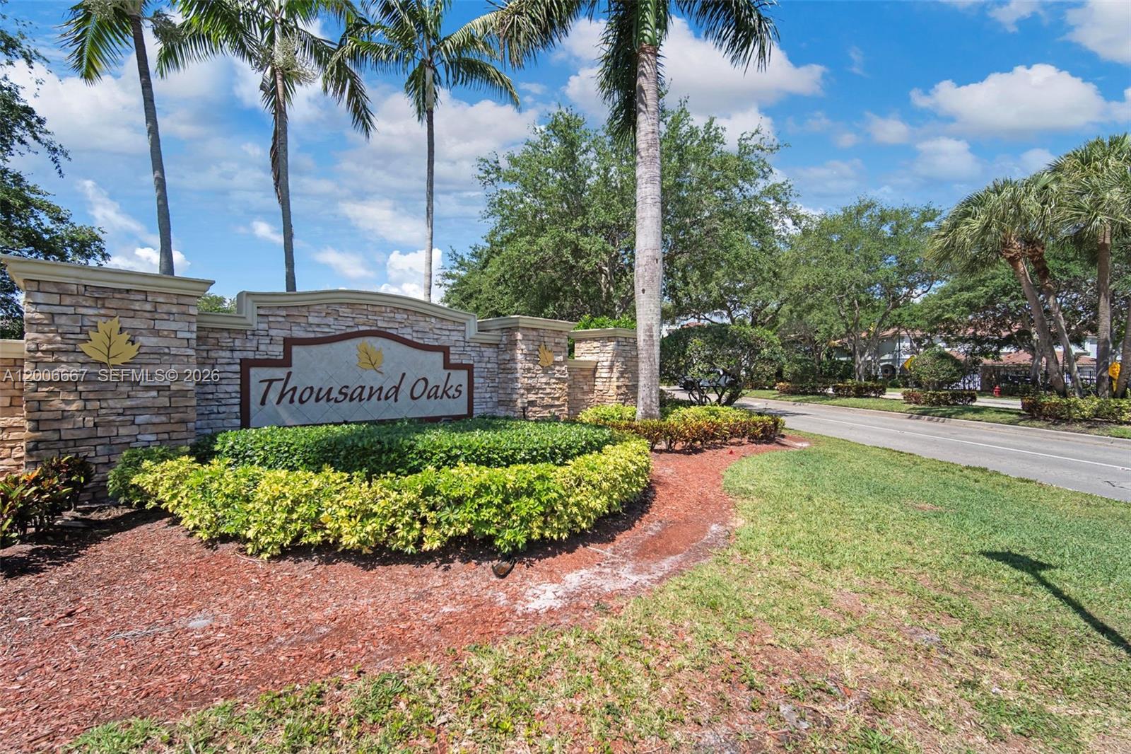 A stone entrance sign for Thousand Oaks stands beside a road with palm trees — 1225 Rosegate Blvd, Riviera Beach FL 33404, RIVIERA BEACH, FL