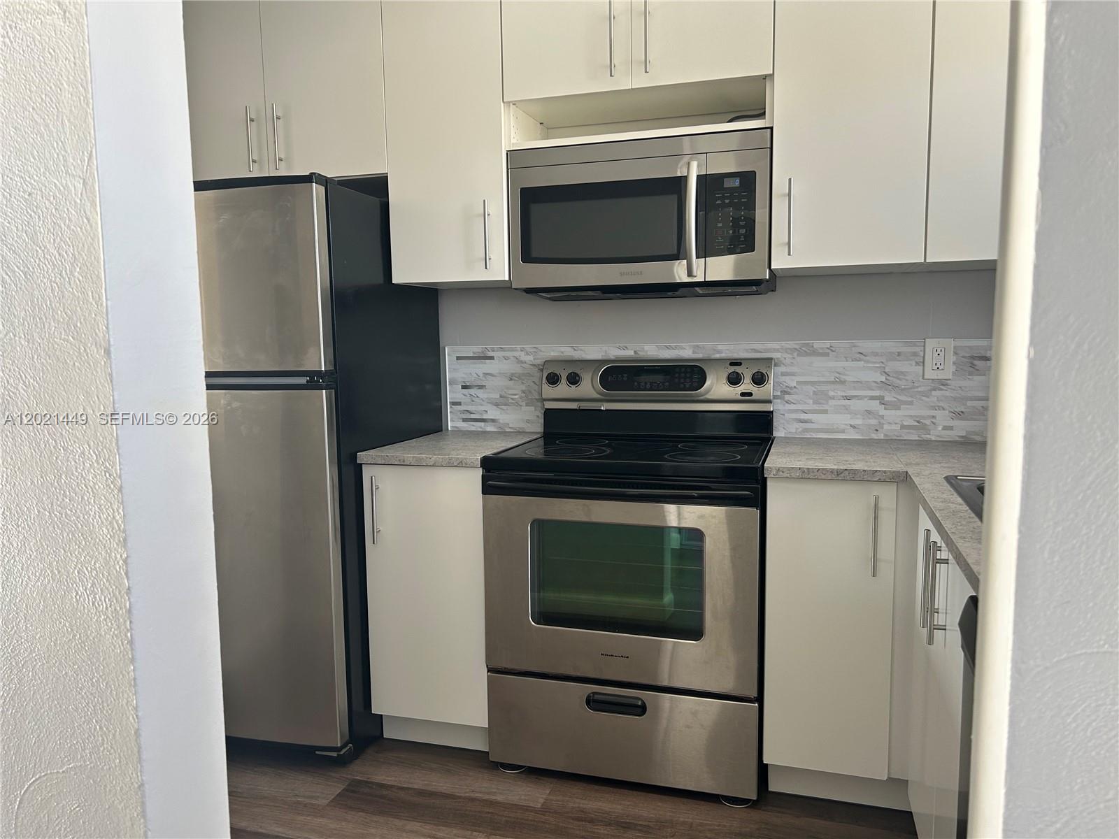 A kitchen features white cabinets, stainless steel appliances, and a gray stone-look backsplash — 2831 E Sunrise Lakes Dr # 309, Sunrise FL 33322, SUNRISE, FL