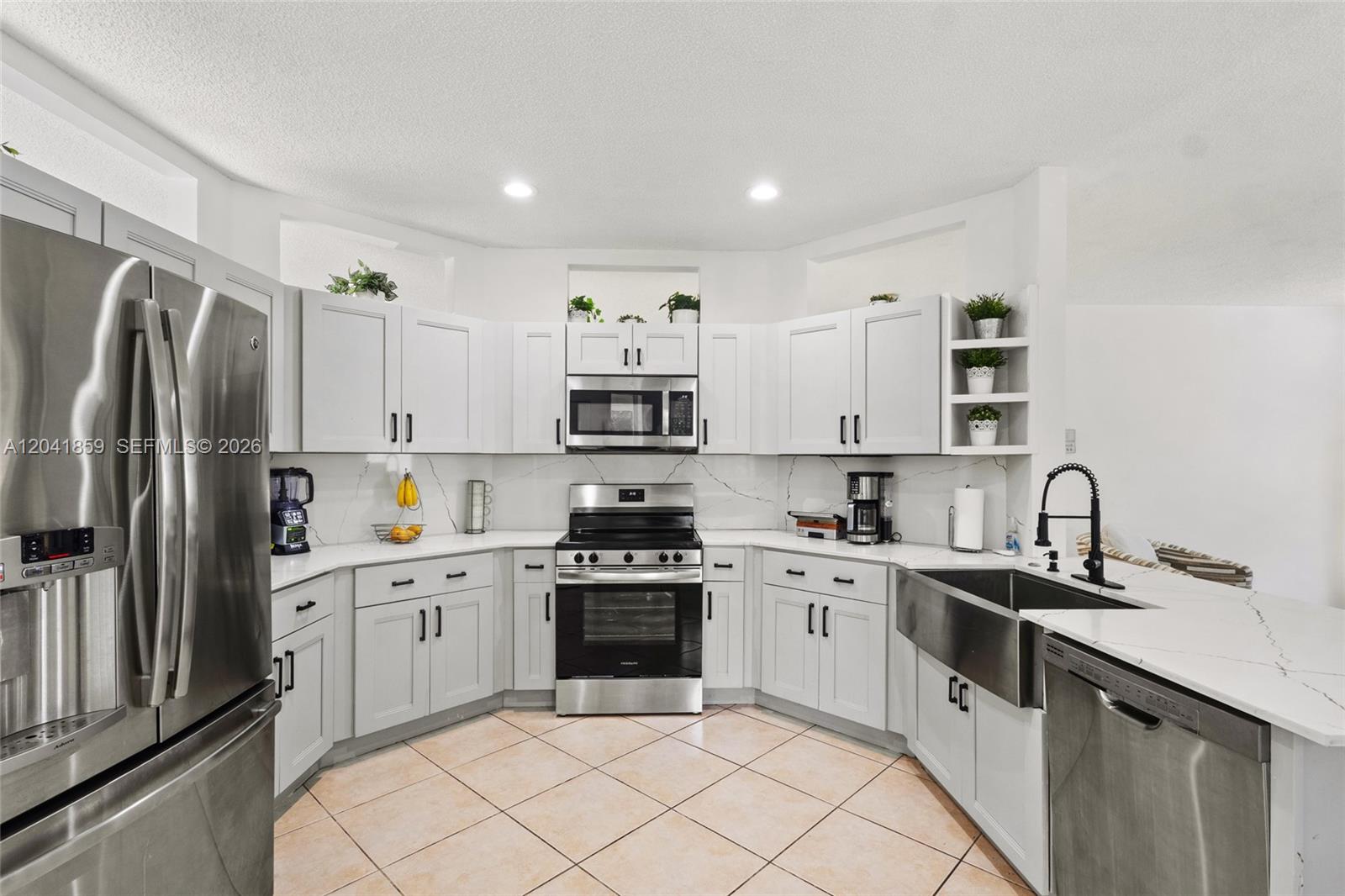 A kitchen features light gray cabinets, stainless steel appliances, a farmhouse sink, and tile flooring — 18222 SW 27th Street, Miramar FL 33029, MIRAMAR, FL