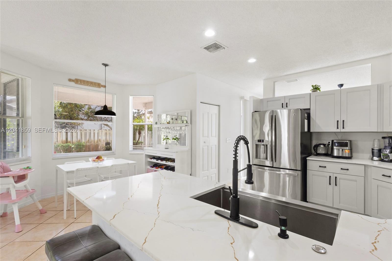 A modern kitchen features white cabinetry, a marble-topped island, stainless steel appliances, and dining area — 18222 SW 27th Street, Miramar FL 33029, MIRAMAR, FL