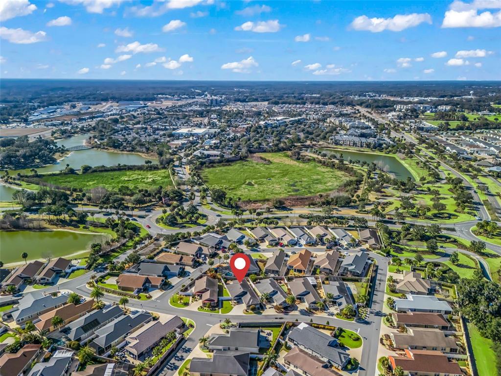An aerial view shows a residential neighborhood with houses, streets, and nearby ponds and fields — 3698 ROBERTSON WAY, THE VILLAGES, FL