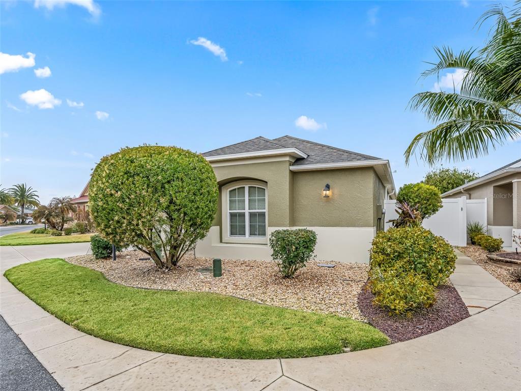 A single-story house with tan stucco walls, a shingled roof, and landscaped front yard — 3698 ROBERTSON WAY, THE VILLAGES, FL