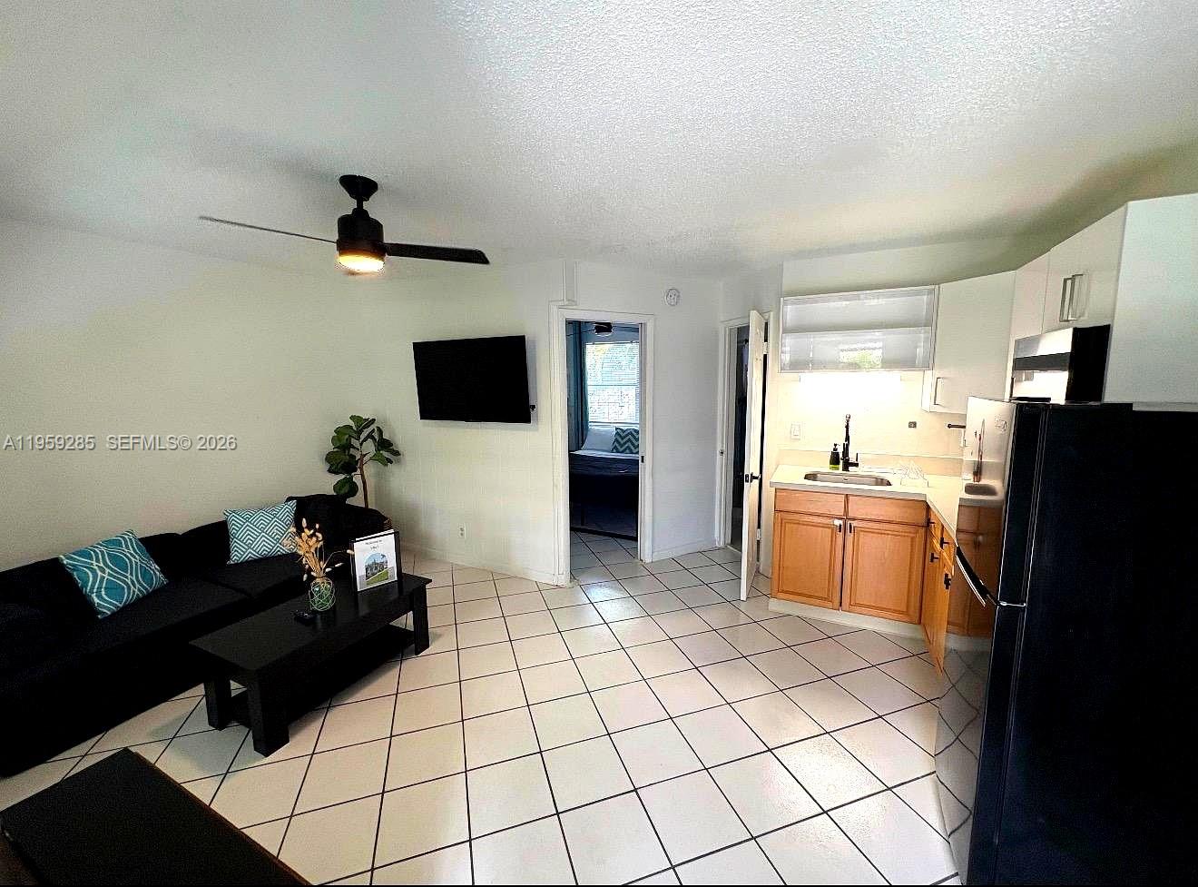 A living room with tile floors and a ceiling fan opens into a small kitchen — 3210 Canal Dr # 7, Pompano Beach FL 33062, POMPANO BEACH, FL