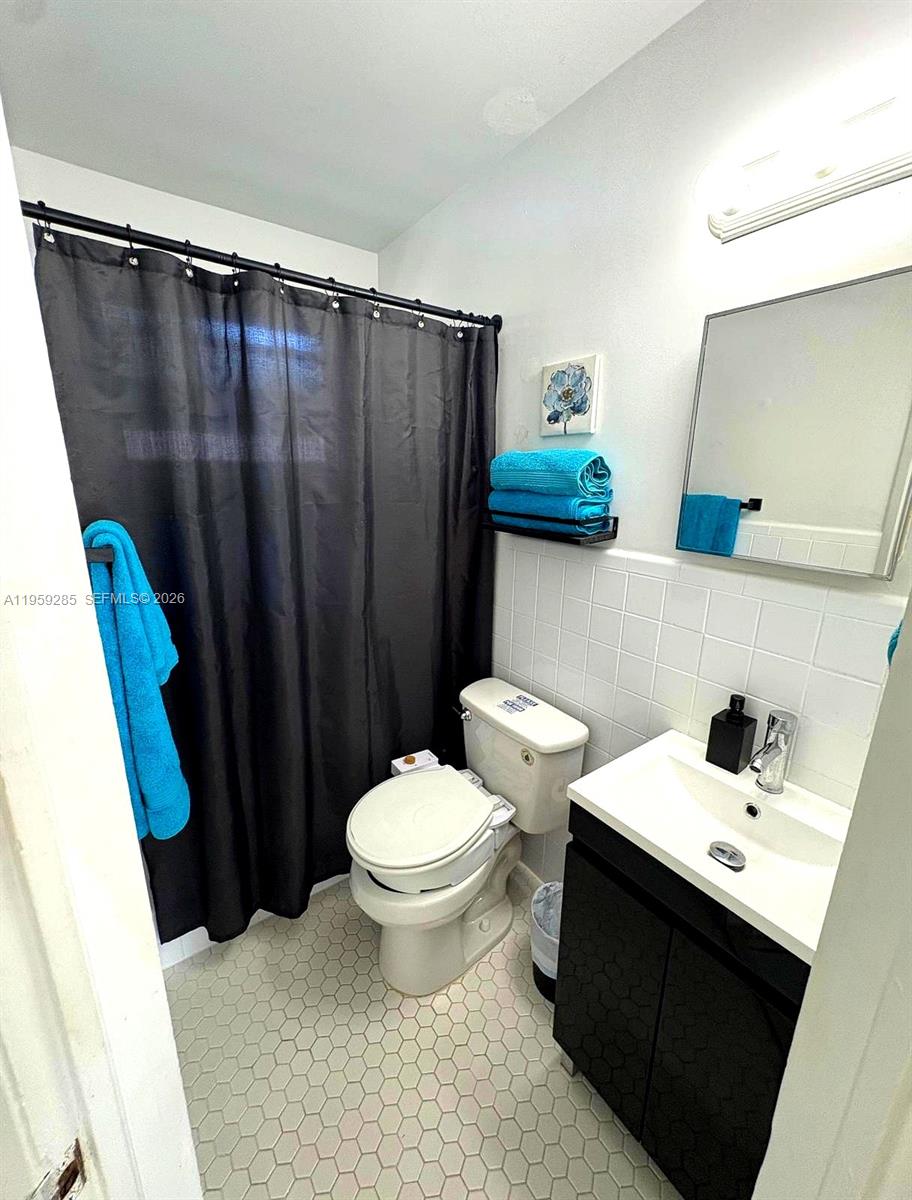 A small bathroom features a black shower curtain, a white toilet, and a vanity sink — 3210 Canal Dr # 7, Pompano Beach FL 33062, POMPANO BEACH, FL