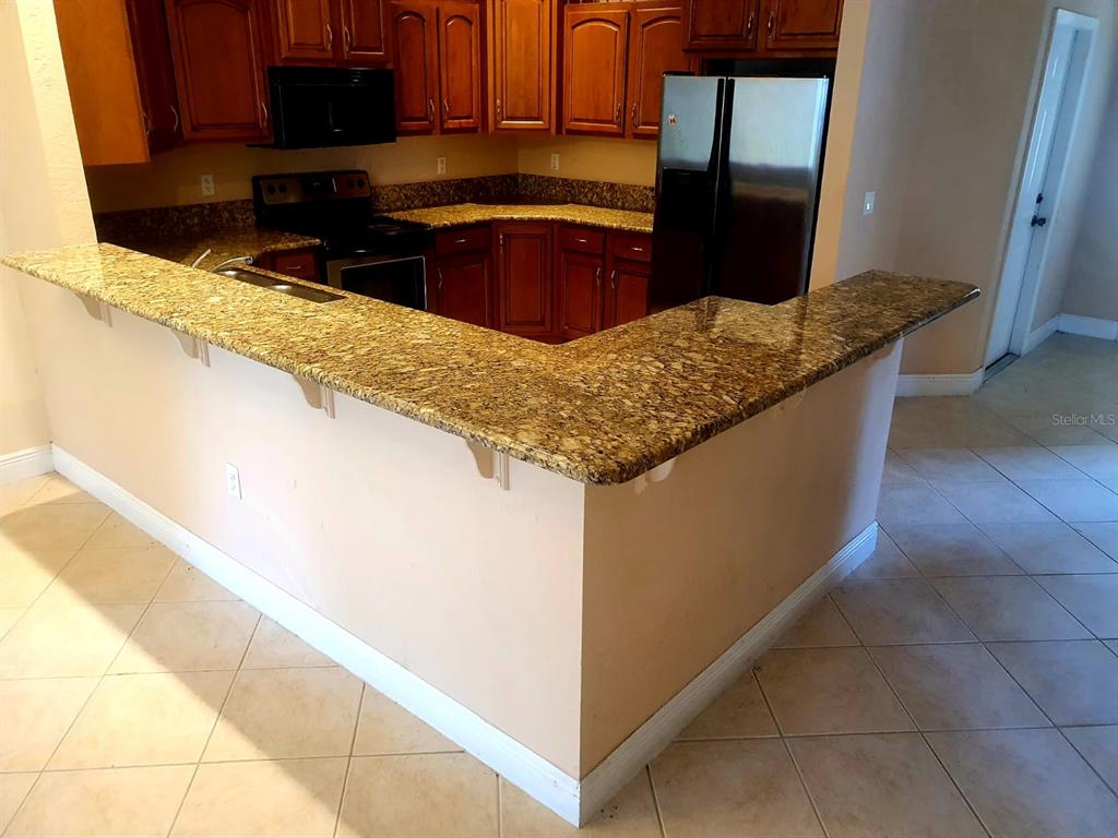 A kitchen features wood cabinets, granite countertops, and a breakfast bar overlooking a tiled floor — 4706 MACKEREL DRIVE, SEBRING, FL