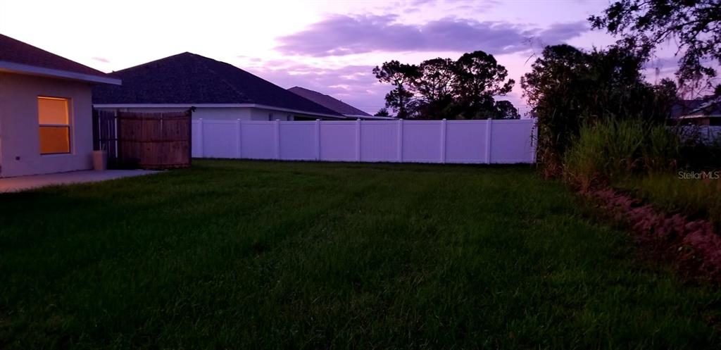 A grassy backyard features a white vinyl fence and a view of neighboring houses — 4706 MACKEREL DRIVE, SEBRING, FL