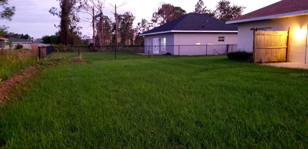 A grassy backyard features a chain-link fence and a view of a neighboring house — 4706 MACKEREL DRIVE, SEBRING, FL